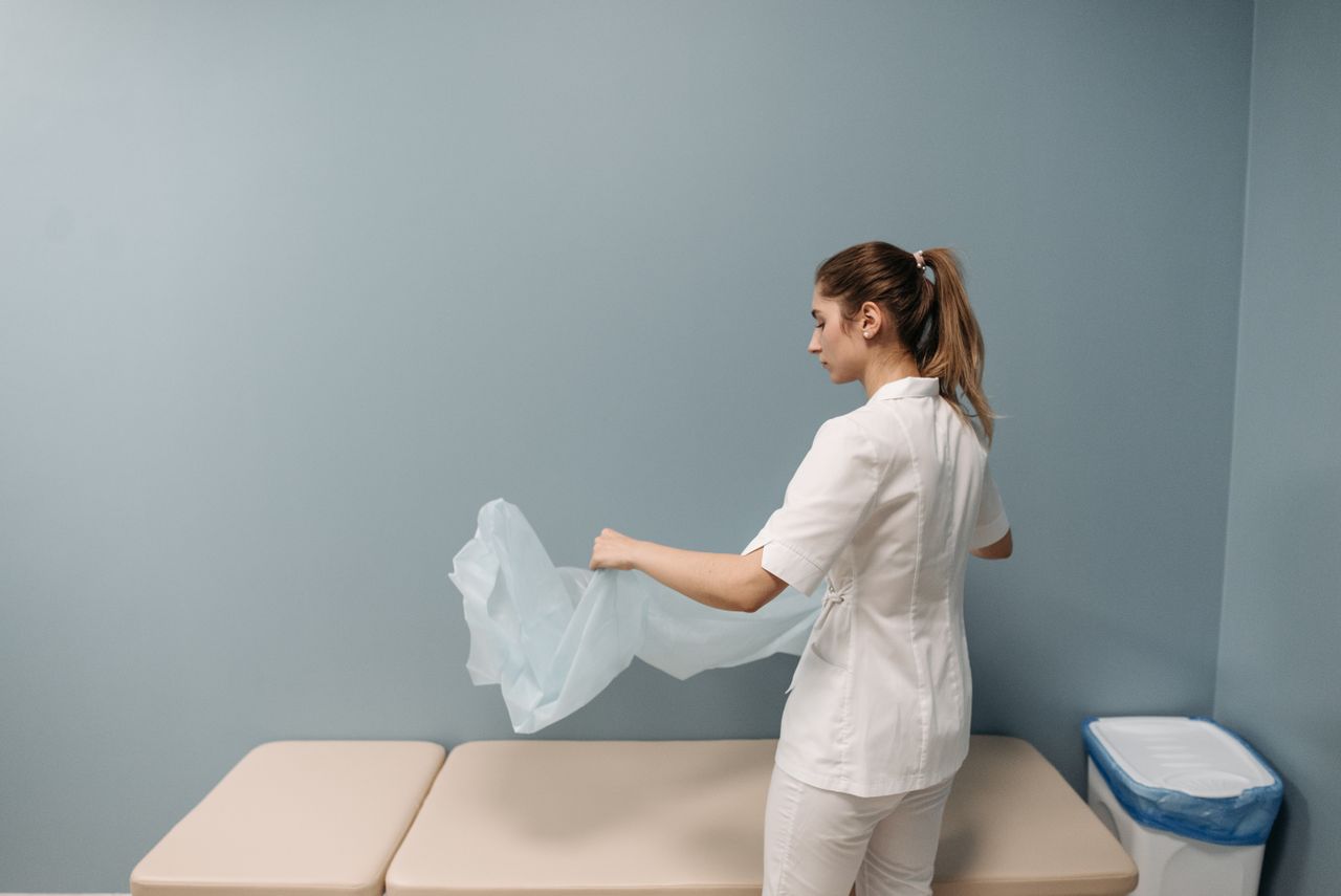 gallery-6 A nurse prepares an examination table in a healthcare facility, ensuring cleanliness and safety.