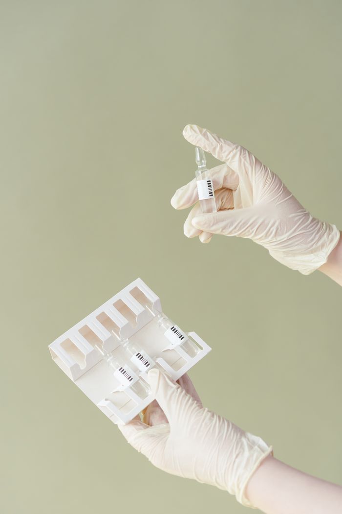 hero-img-02 Medical ampoules being held by gloved hands against a soft green background.